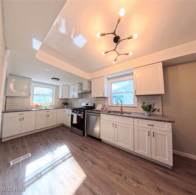 Kitchen with white cabinets, tasteful backsplash, stainless steel appliances, dark wood finished floors, and wall chimney range hood