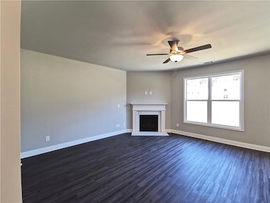 Unfurnished living room featuring dark wood-style floors, a ceiling fan, and a fireplace with raised hearth