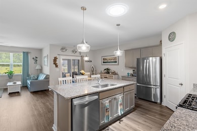 Kitchen with stainless steel appliances, gray cabinets, dark wood-style flooring, light stone counters, and a kitchen island with sink
