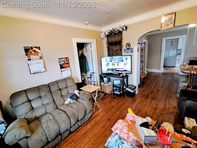 Living area with ornamental molding, wood finished floors, and arched walkways