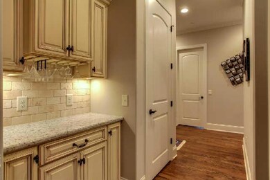 The Butlers pantry is located in the hall between the kitchen and the DR.   Features include custom glazed cabinetry, granite, tiled backsplash, under cabinet wine glass holder, and under cabinet lighting.