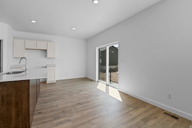 Kitchen featuring recessed lighting, light wood finished floors, light stone counters, white cabinetry, and dark brown cabinetry