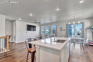 Kitchen with dark wood-type flooring, white cabinets, a breakfast bar area, a kitchen island with sink, and recessed lighting