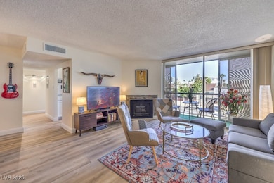 Living area with a textured ceiling, a fireplace, light wood-style flooring, and floor to ceiling windows