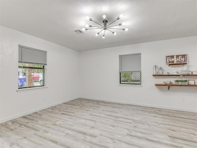 Empty room with light wood-style floors, a chandelier, and a textured ceiling