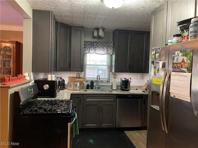 Kitchen with black appliances, decorative backsplash, light stone counters, and light wood-style flooring