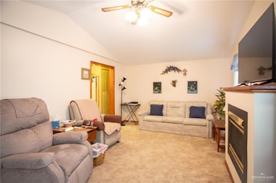 Living area with a fireplace, light colored carpet, a ceiling fan, and lofted ceiling