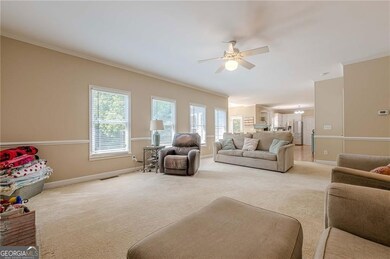 Living room featuring a ceiling fan, baseboards, light colored carpet, and crown molding