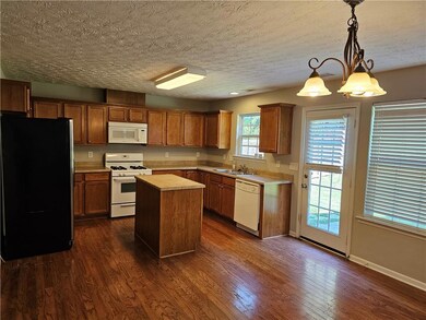 Kitchen featuring white appliances, dark wood finished floors, light countertops, a kitchen island, and pendant lighting