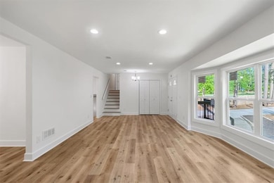 Unfurnished living room featuring a chandelier, light wood-style floors, recessed lighting, and stairway