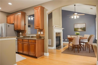 Kitchen with ceiling fan, vaulted ceiling, light wood-style floors, brown cabinets, and dark stone countertops