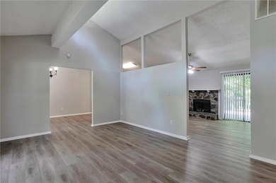 Unfurnished room featuring a ceiling fan, wood finished floors, and a stone fireplace