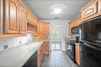 Kitchen featuring black appliances, light countertops, tasteful backsplash, and a textured ceiling