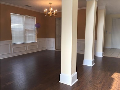 Unfurnished dining area featuring decorative columns, a chandelier, crown molding, wood finished floors, and a wainscoted wall