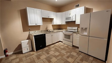 Kitchen featuring white appliances, a sink, white cabinetry, and baseboards