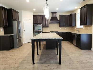 Kitchen with custom exhaust hood, decorative backsplash, appliances with stainless steel finishes, light stone countertops, and recessed lighting