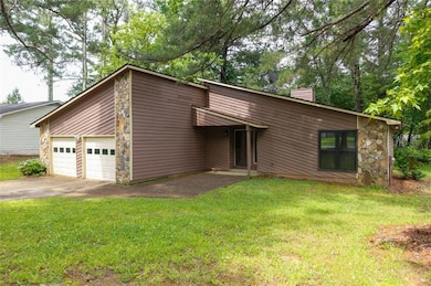 Mid-century home featuring a garage, a chimney, stone siding, and concrete driveway