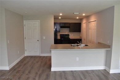Kitchen with hardwood / wood-style floors, black appliances, kitchen peninsula, sink, and dark brown cabinetry