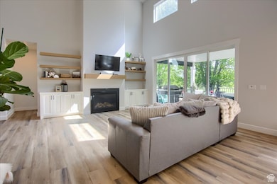 Living area with a towering ceiling, a glass covered fireplace, and light wood-style floors