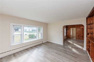 Unfurnished room with a baseboard heating unit, light wood finished floors, and arched walkways