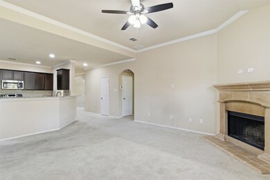 Unfurnished living room with a fireplace with raised hearth, arched walkways, light carpet, crown molding, and ceiling fan