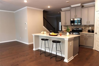 Kitchen featuring stainless steel appliances, gray cabinets, backsplash, a kitchen bar, and crown molding