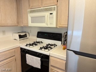 Kitchen with tile counters, gas range oven, freestanding refrigerator, and white microwave