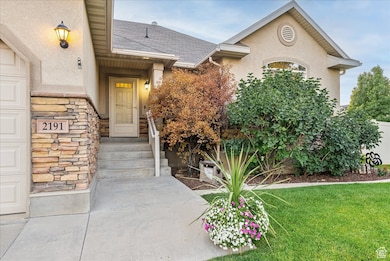 Property entrance with stucco siding, roof with shingles, stone siding, a lawn, and a garage