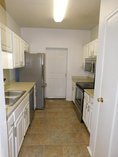 Kitchen with light countertops, stainless steel appliances, white cabinetry, and stone finish floors