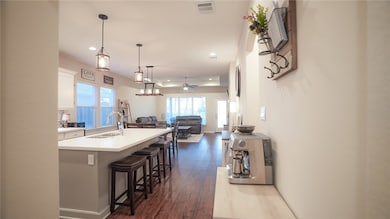 Kitchen featuring white cabinets, an island with sink, open floor plan, dark wood-type flooring, and pendant lighting