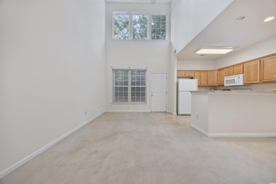Kitchen featuring white appliances, light colored carpet, a towering ceiling, light countertops, and a peninsula