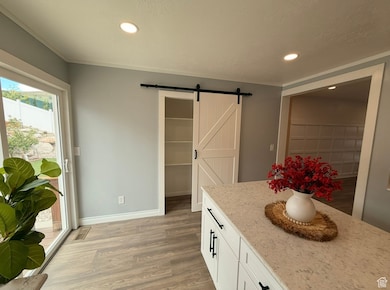 Kitchen with a barn door, light wood finished floors, light stone countertops, white cabinets, and recessed lighting