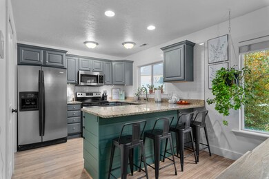 Kitchen with appliances with stainless steel finishes, a kitchen bar, light stone countertops, light wood-style floors, and a peninsula