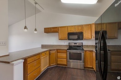 Kitchen featuring black appliances, decorative light fixtures, dark wood-type flooring, brown cabinetry, and lofted ceiling