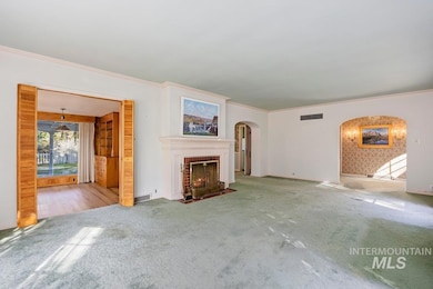 Unfurnished living room with crown molding, a brick fireplace, carpet flooring, and arched walkways