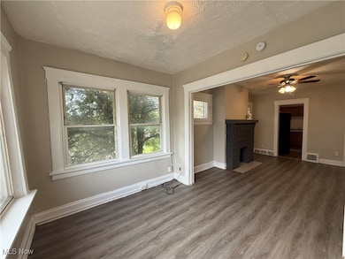 Unfurnished living room with wood finished floors, a textured ceiling, a brick fireplace, and a ceiling fan