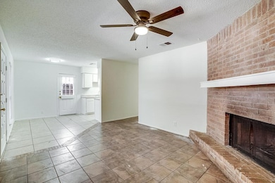 Unfurnished living room featuring a textured ceiling, light tile patterned floors, ceiling fan, and a brick fireplace