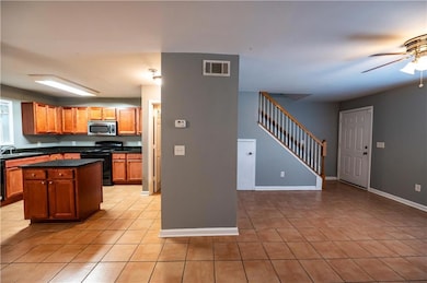 Kitchen featuring black appliances, dark countertops, a ceiling fan, light tile patterned floors, and a center island