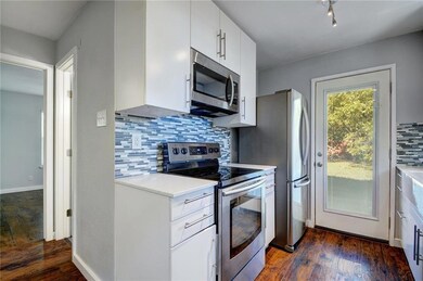 Kitchen featuring stainless steel appliances, white cabinetry, dark wood-style floors, and backsplash