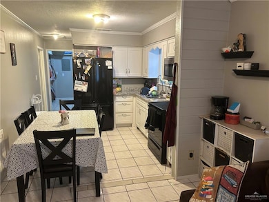 Kitchen with white cabinets, black appliances, a textured ceiling, ornamental molding, and light tile patterned floors