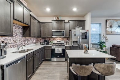 Kitchen featuring stainless steel appliances, a kitchen breakfast bar, backsplash, a center island, and light wood-style flooring