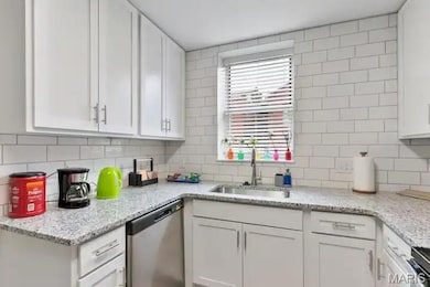 Kitchen featuring stainless steel dishwasher, a sink, and white cabinets