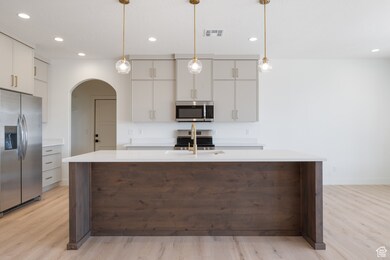 Kitchen with stainless steel appliances, an island with sink, arched walkways, recessed lighting, and hanging light fixtures