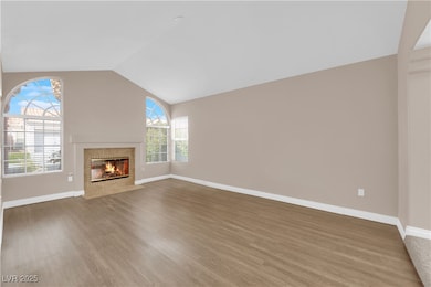 Unfurnished living room with a fireplace, vaulted ceiling, and wood finished floors