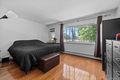 Bedroom featuring light wood-type flooring, a baseboard radiator, and a wall mounted air conditioner