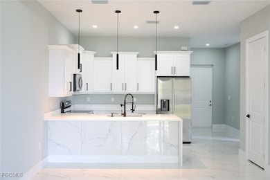 Kitchen featuring white cabinets, appliances with stainless steel finishes, light stone counters, light marble finish floors, and a peninsula