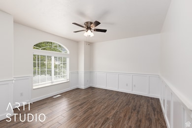 Office with a decorative wall, a wainscoted wall, dark wood-type flooring, and ceiling fan