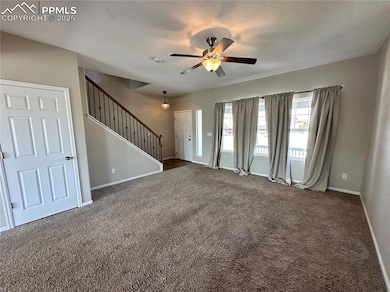 Unfurnished living room featuring stairway, dark colored carpet, and ceiling fan