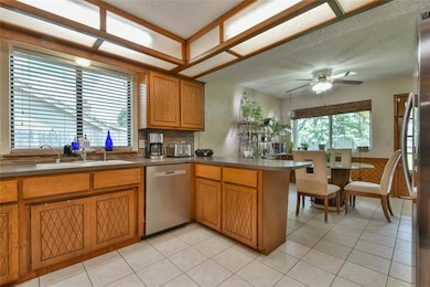 Kitchen featuring dishwasher, a peninsula, brown cabinetry, a ceiling fan, and a textured ceiling