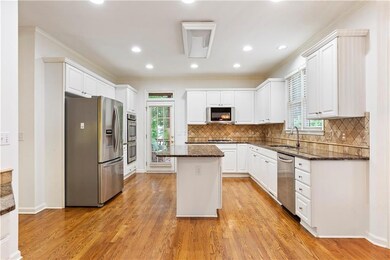 Kitchen featuring stainless steel appliances, a kitchen island, white cabinets, dark stone countertops, and light wood-style floors